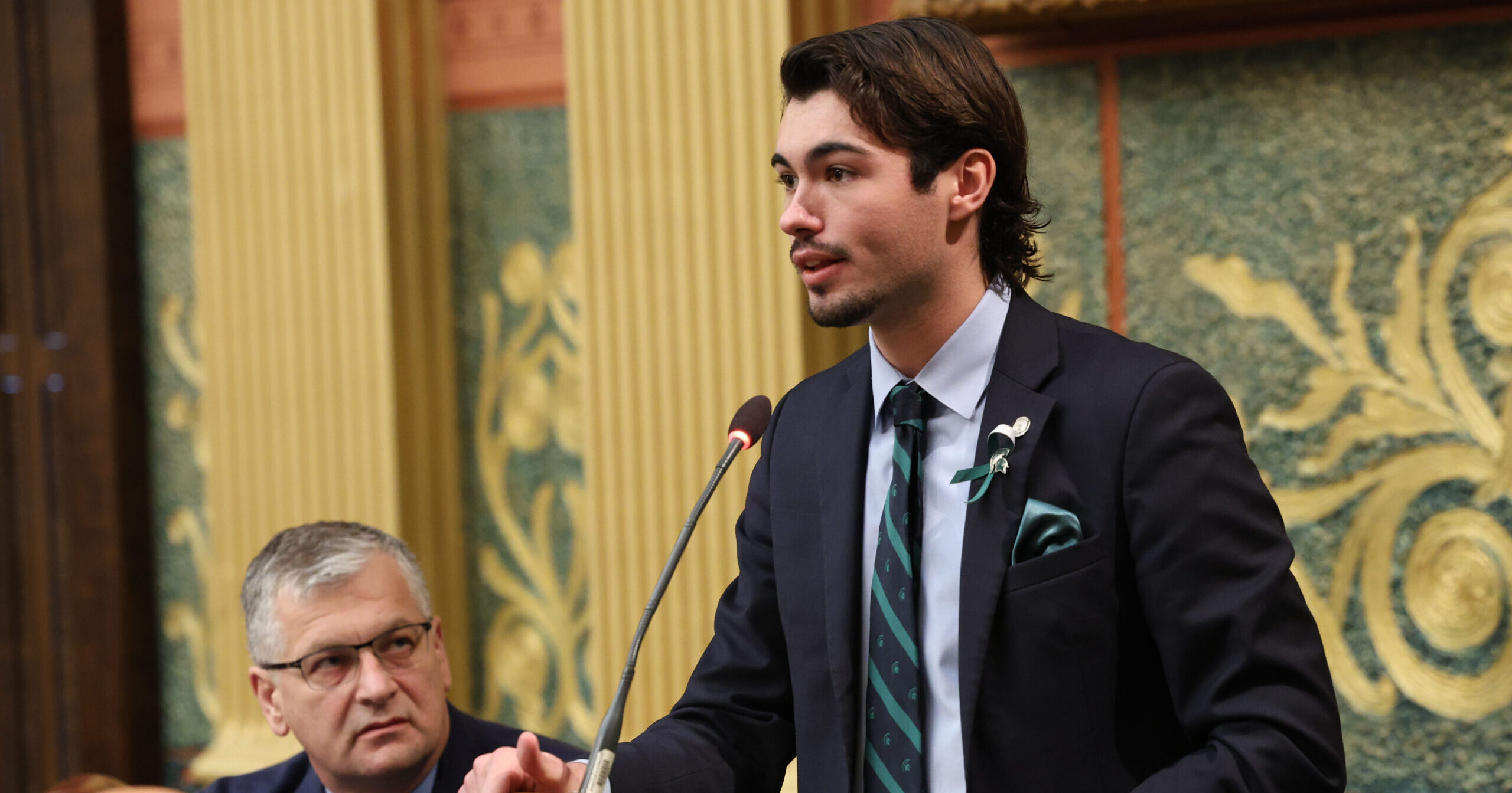 State Rep. Jasper Martus stands speaking on the house floor at the podium