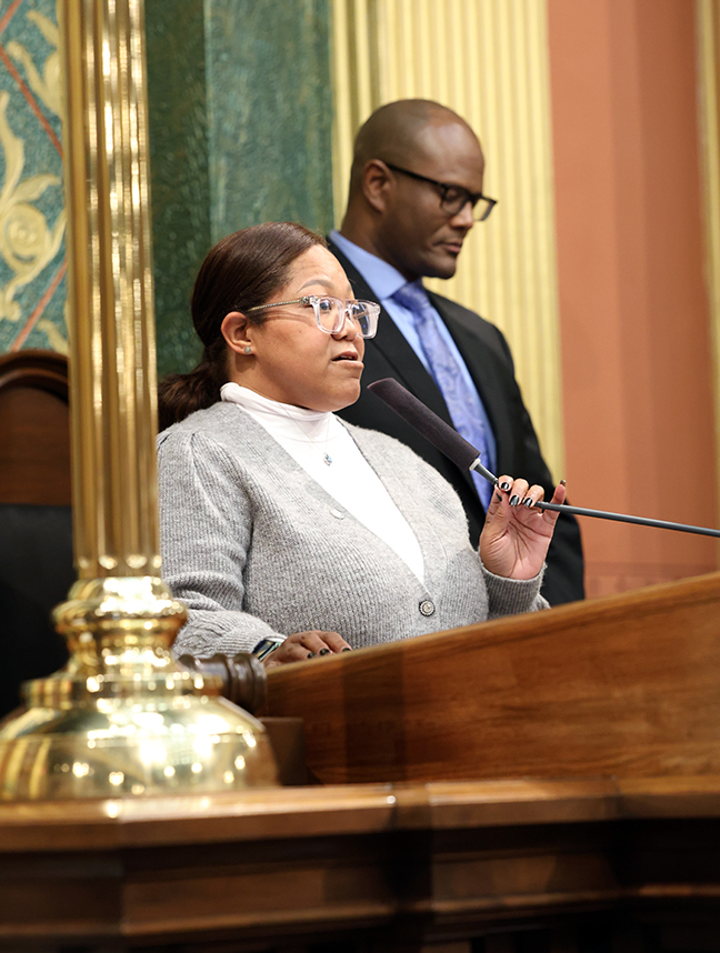 Rep. Edwards stands on the Michigan House rostrum with Speaker Joe Tate behind her.