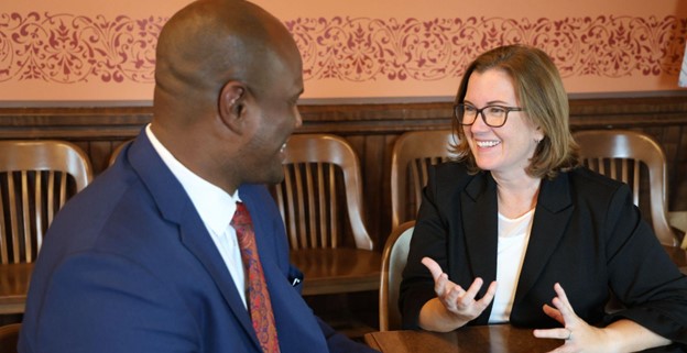 Rep. Natalie Price speaks with Speaker Joe Tate while sitting at a table in the Michigan Capitol.