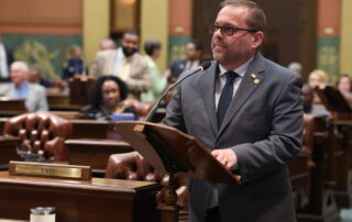 Representative Mike McFall speaks at a podium on the floor of Michigan House of Representatives.