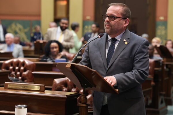 Representative Mike McFall speaks at a podium on the floor of Michigan House of Representatives.