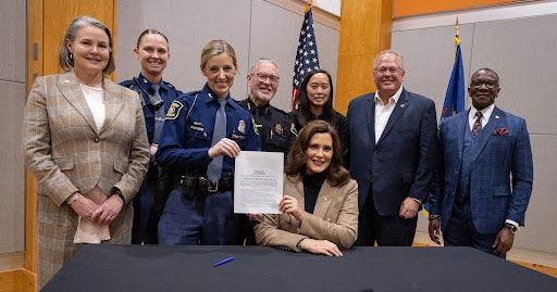 State Rep. Amos O’Neal (D-Saginaw), right, and state Sen. Sue Shink (D-Northfield Township), left, stand with Michigan State Police officers and others after Gov. Gretchen Whitmer signed legislation that bans convicted domestic abusers from owning firearms for a set number of years on Nov. 20, 2023, in Kalamazoo.