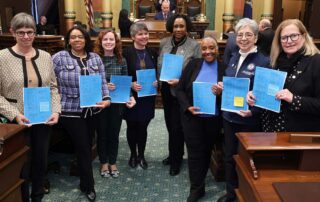 Lawmakers stand together to introduce the pay equity bill package on the Michigan House of Representatives floor on March 19, 2024.