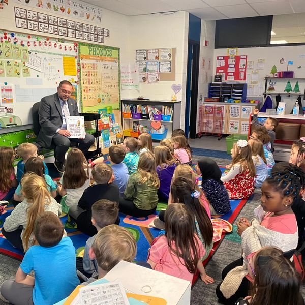 Rep. McFall reads a picture book to elementary schoolers for March is Reading Month.