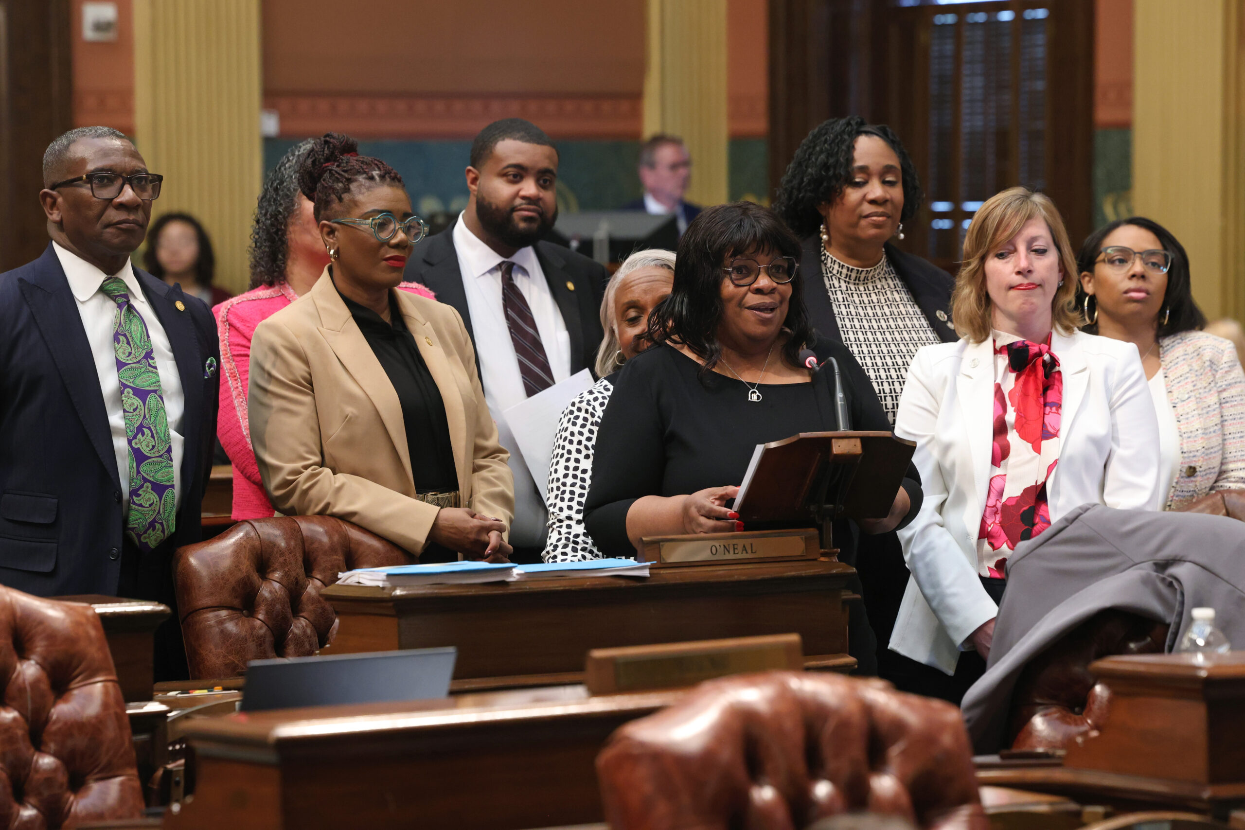 Rep. Brenda Carter stands at the podium on the House floor, presenting the BMHW Resolution. Other Reps. are pictured behind her in support of her speaking.