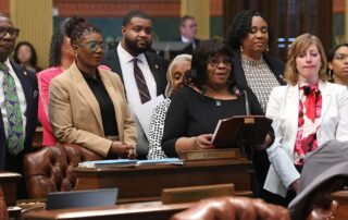 Rep. Brenda Carter stands at the podium on the House floor, presenting the BMHW Resolution. Other Reps. are pictured behind her in support of her speaking.