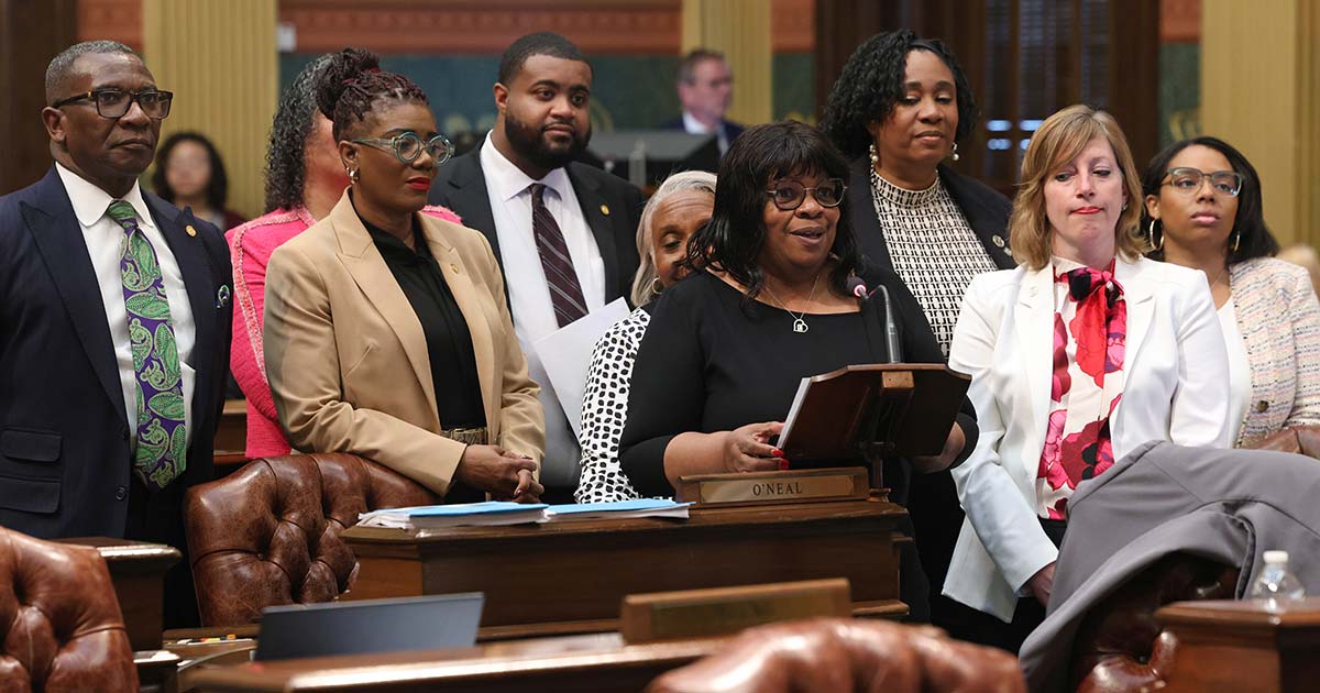 Rep. Brenda Carter stands at the podium on the House floor, presenting the BMHW Resolution. Other Reps. are pictured behind her in support of her speaking.