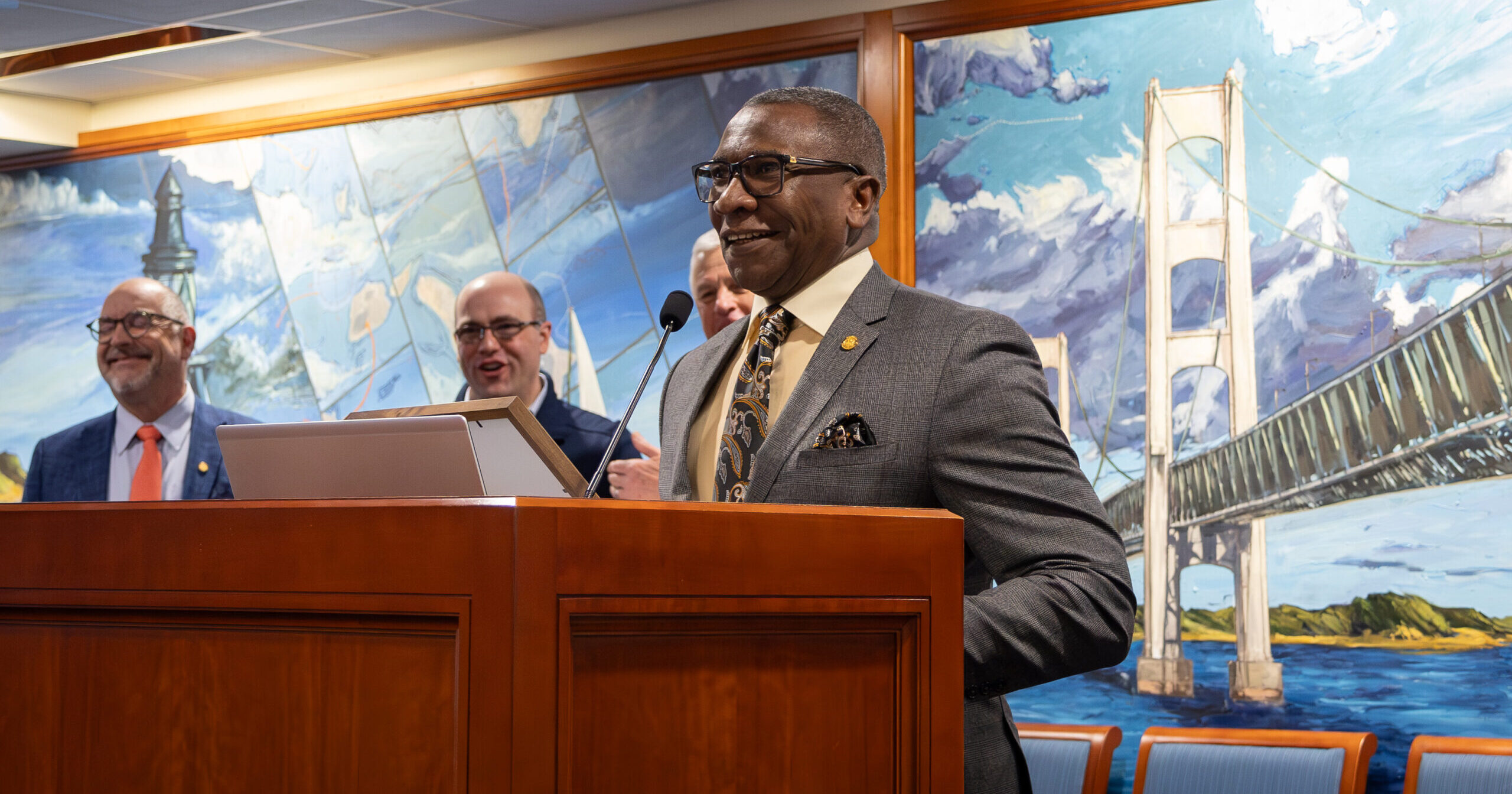 Michigan State Representative Amos O'Neal smiles as he stands smiling as he stands at a potium in the House office building.