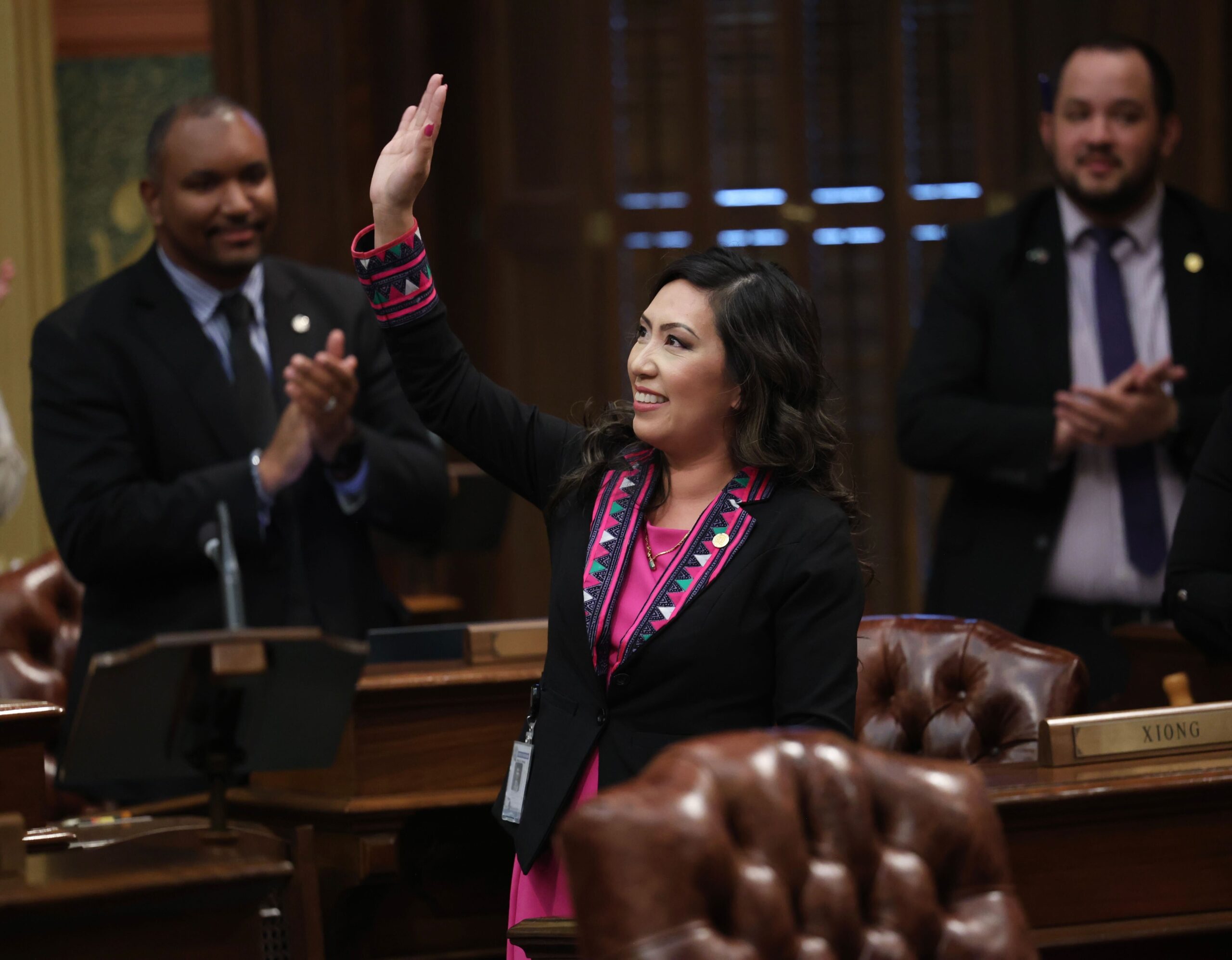 State Representative Mai Xiong waves to the gallery after delivering a speech as her colleagues applaud in the background.