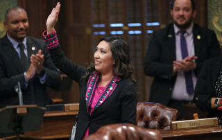 State Representative Mai Xiong waves to the gallery after delivering a speech as her colleagues applaud in the background.