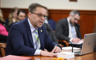 Rep. Mike McFall speaks forcefully while testifying at a table in committee.