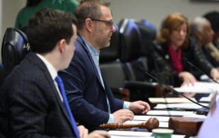 State Rep. McFall chairs the Insurance Committee on the dais, flanked by the clerk and fellow legislators.