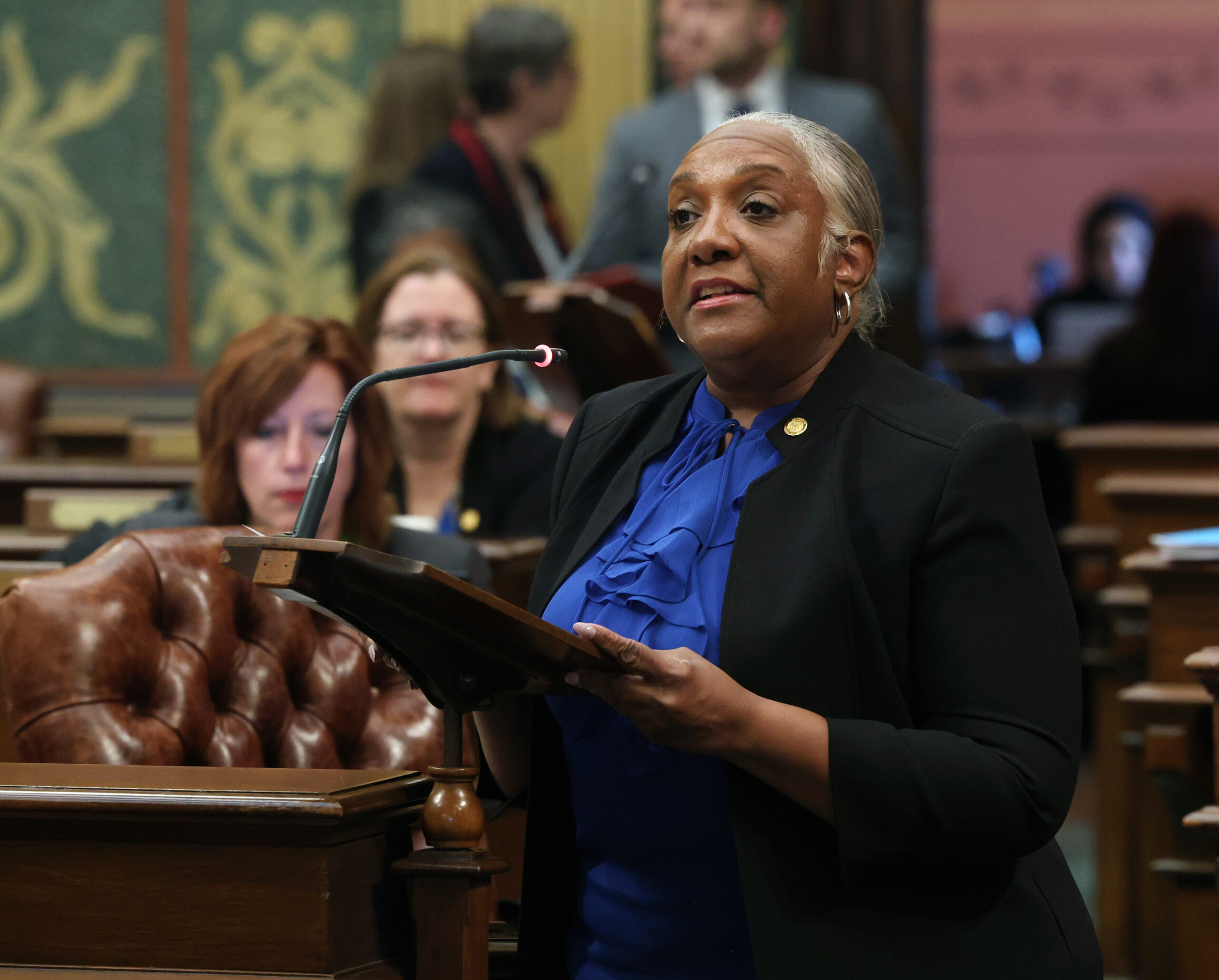 Rep. Helena Scott stands behind a podium, speaking on the House Floor. 
