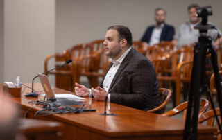 Rep. Farhat testifies in committee at a table.