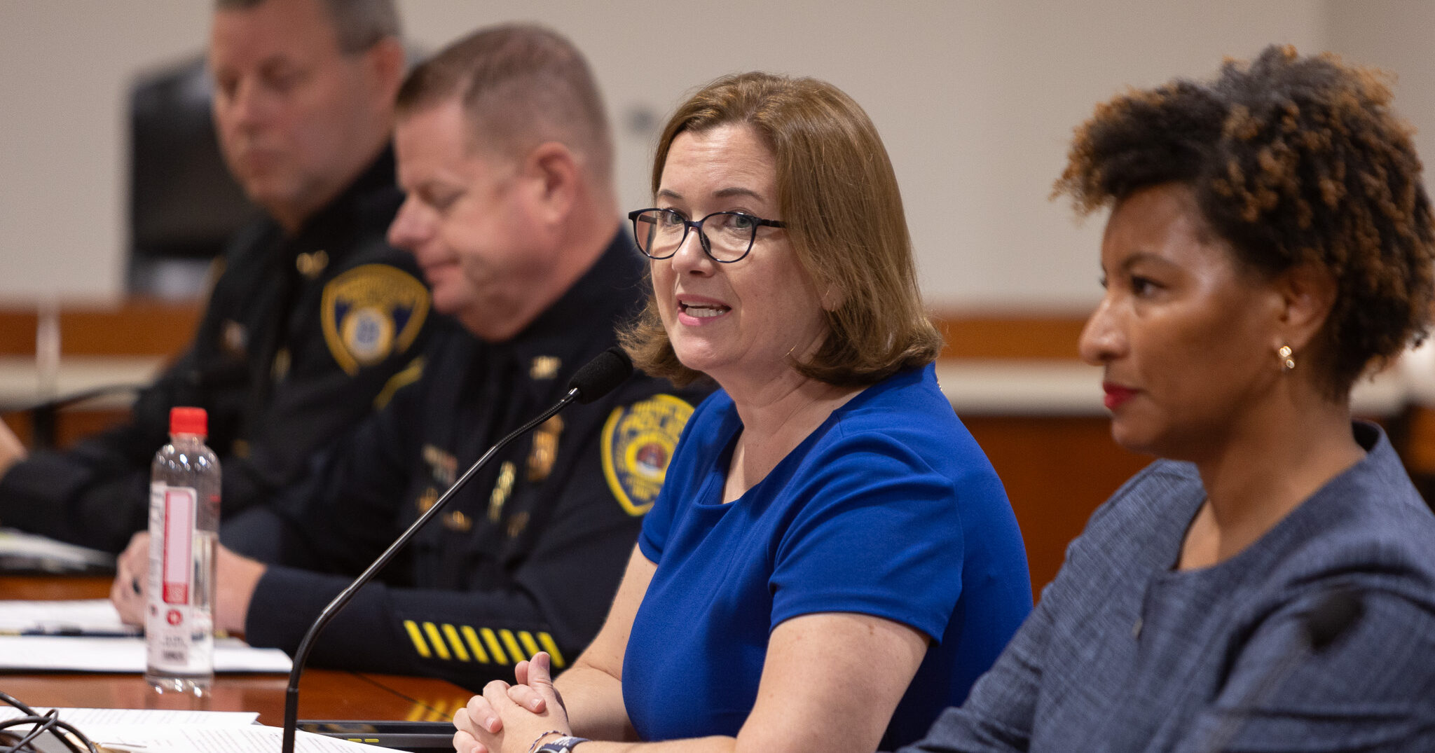 State Rep. Natalie Price testifies on her House Bill 5696 into a microphone at a table while surrounded by local officials.