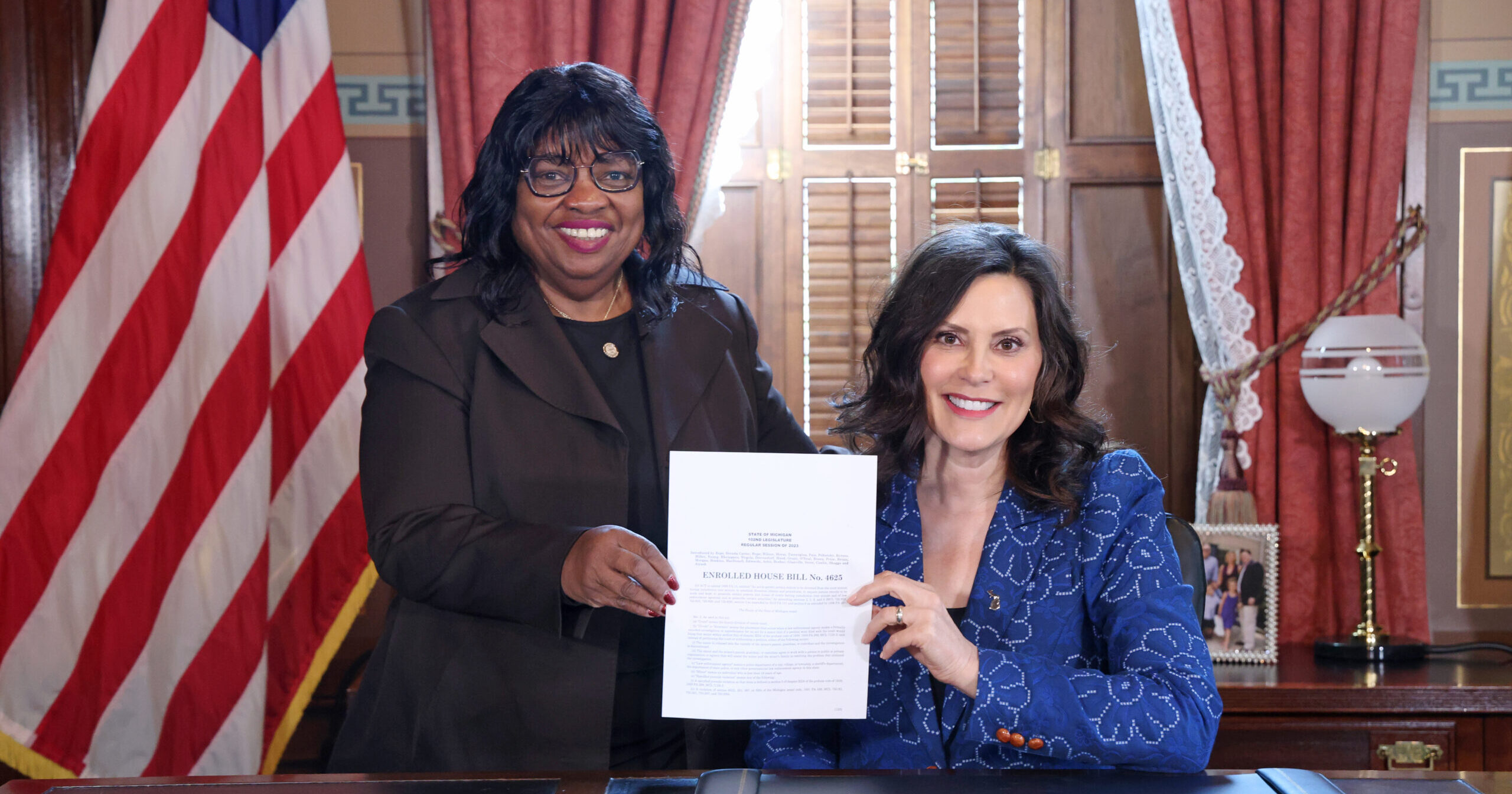 state Rep. Brenda Carter standing next to Gov. Gretchen Whitmer while they hold newly signed legislation