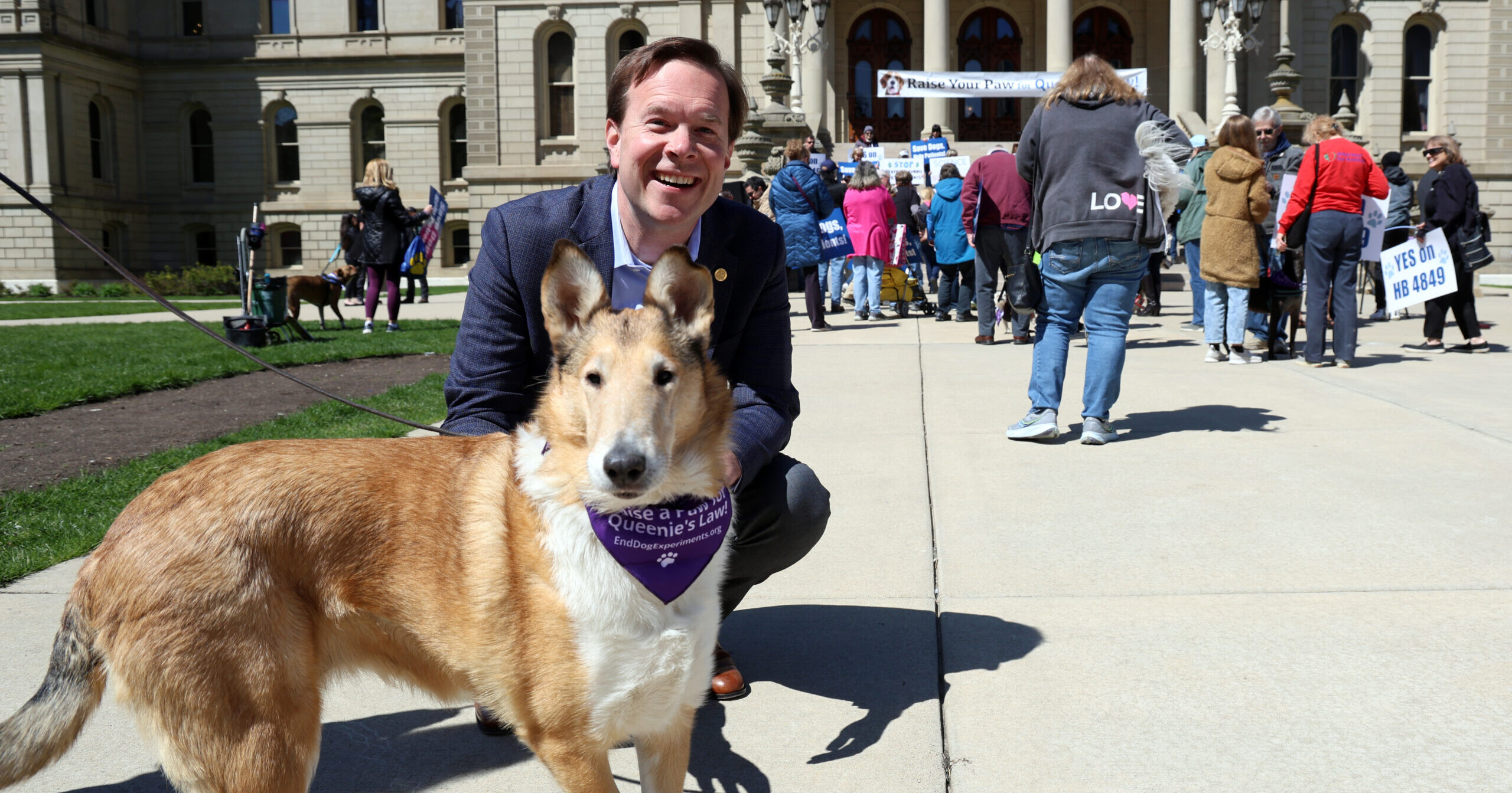 Michigan state Representative Matt Koleszar poses with a dog at a rally for his bill, or "Queenie's Law," on the steps of the Michigan Capitol Building.