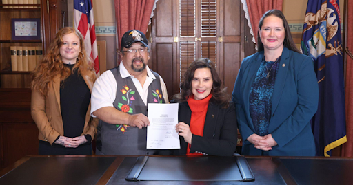 State Representative Rheingans stands next Michigan governor Gretchen Witmer. The governor holds the recently signed bill with Roger LaBine, elder and rice keeper in the Lac Vieux Desert Band of Lake Superior Chippewa.