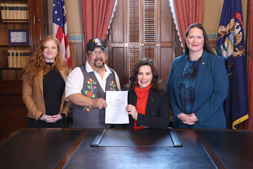 State Representative Rheingans stands next Michigan governor Gretchen Witmer. The governor holds the recently signed bill with Roger LaBine, elder and rice keeper in the Lac Vieux Desert Band of Lake Superior Chippewa.