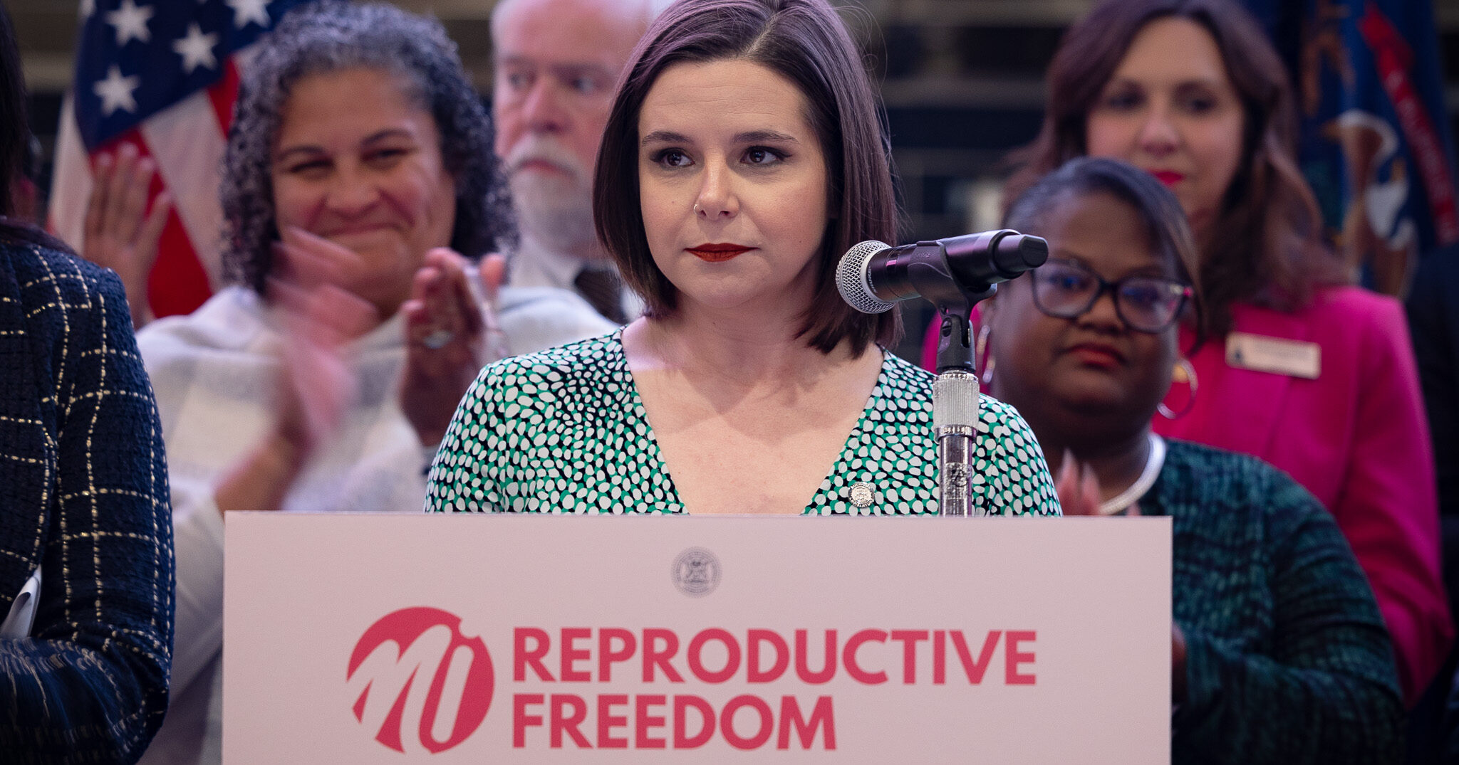 House Speaker Pro Tem Laurie Pohutsky stands behind a pink podium and sign that reads "reproductive Freedoms"