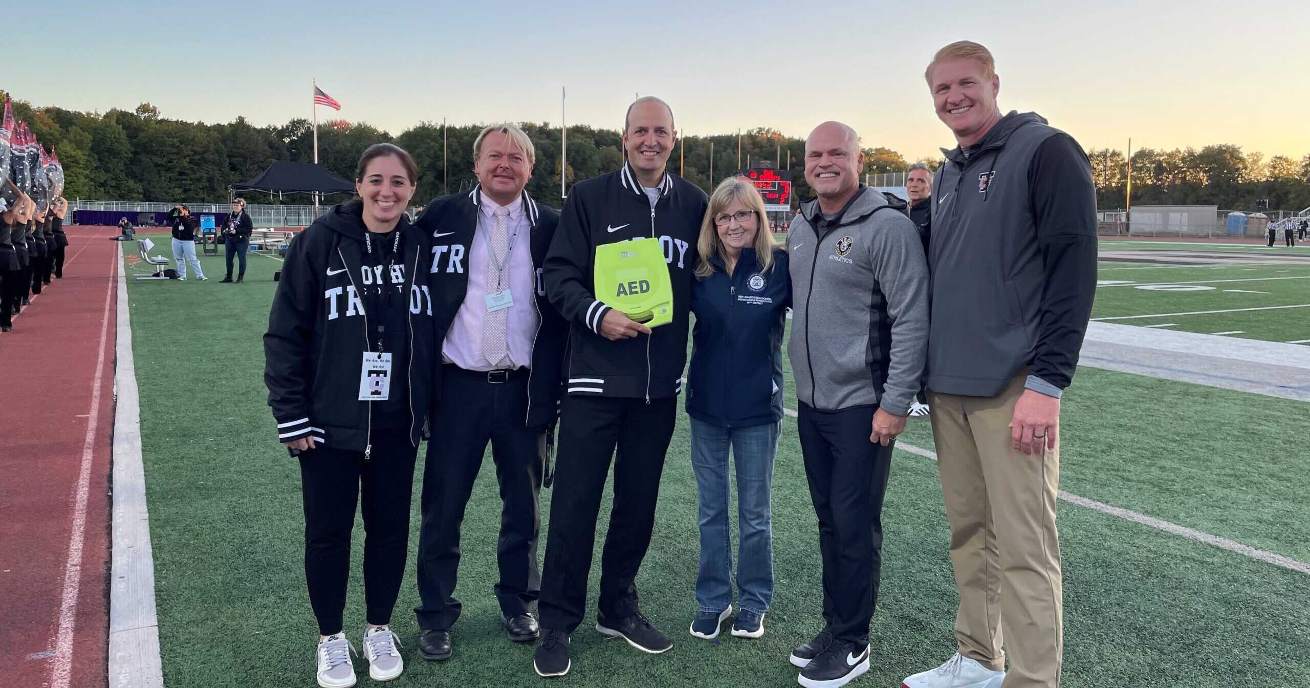 Troy High School Vice Principal Brennan, Vice Principal House, Principal Roncone, Michigan State Rep. MacDonell, Superintendent Machesky and Athletic Director Jansen at the presentation of an automated external defibrillator (AED) at a home football game.