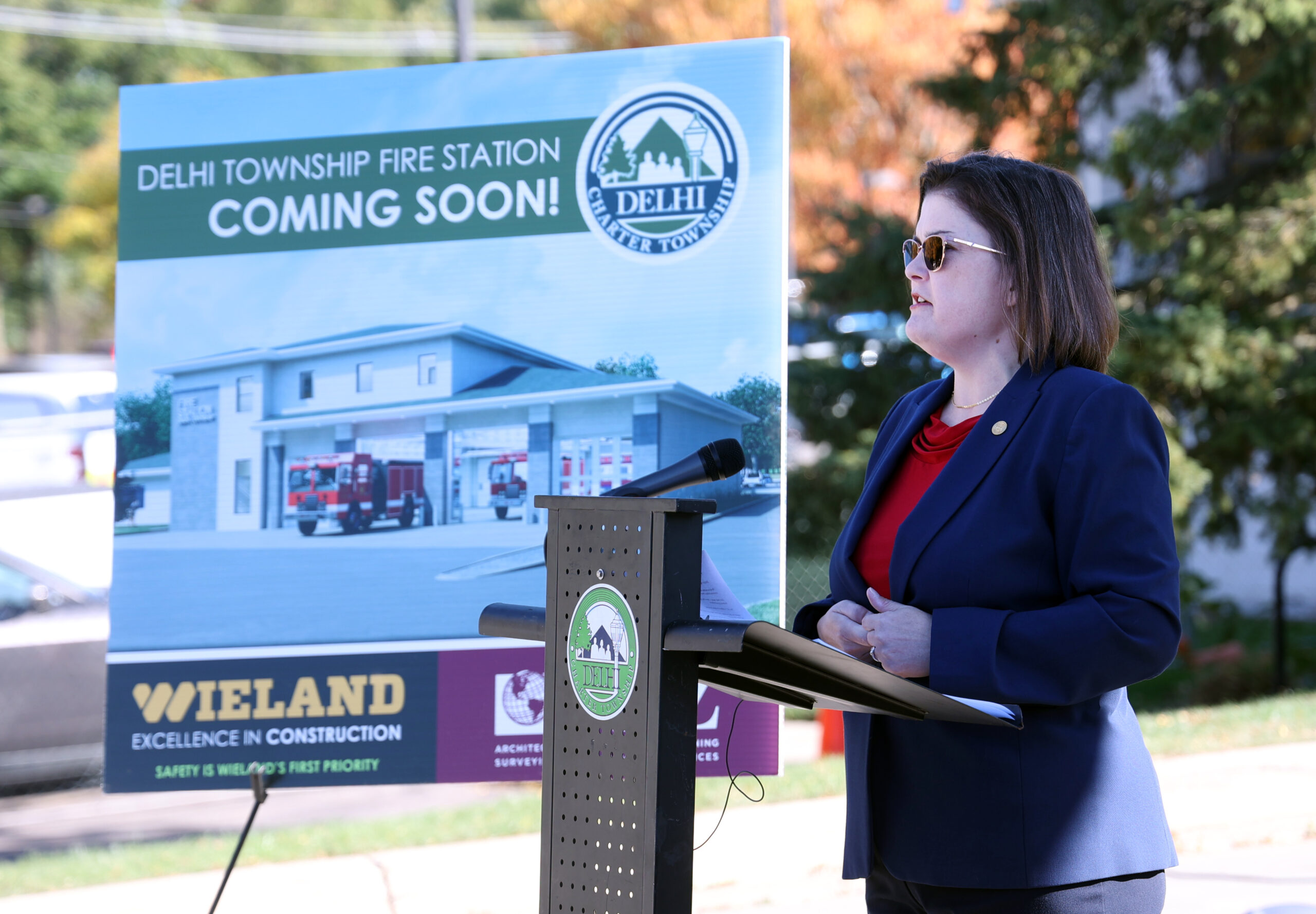 Michigan State Representative Kara Hope speaks behind a podium at a groundbreaking ceremony for renovations at the Delhi Township Fire Station.