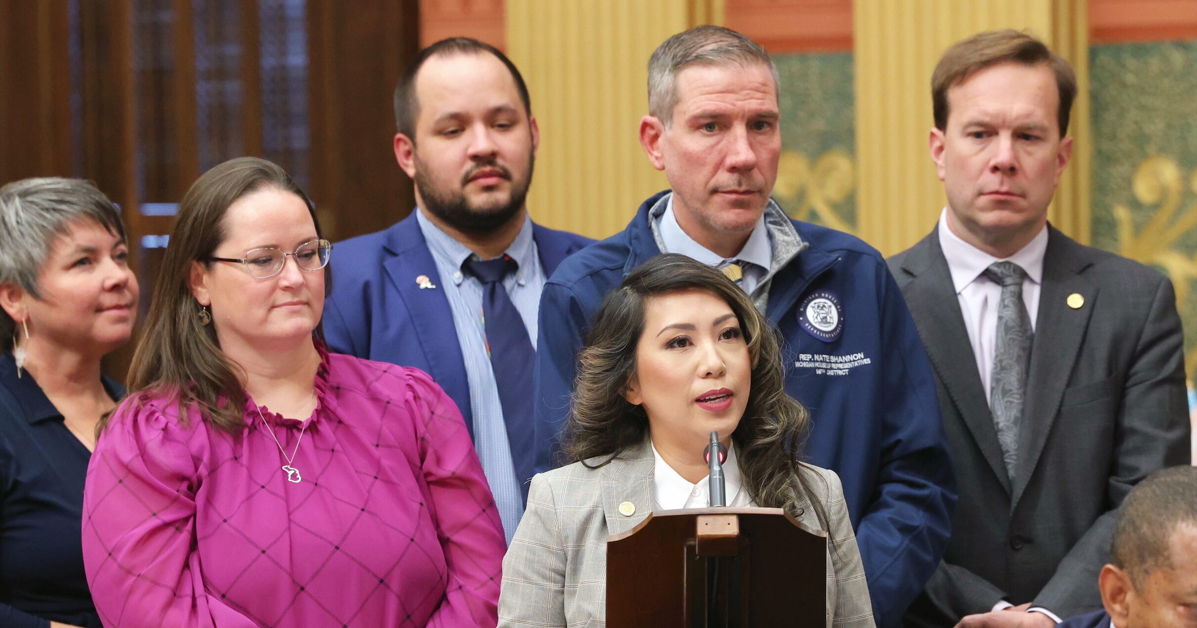 Michigan State Representative Mai Xiong speaking on the House Floor in front of a group of supporting colleagues.