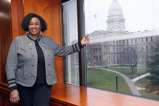 Michigan State Representative Stephanie A. Young standing in front of a window with the Michigan state Capitol in the background.