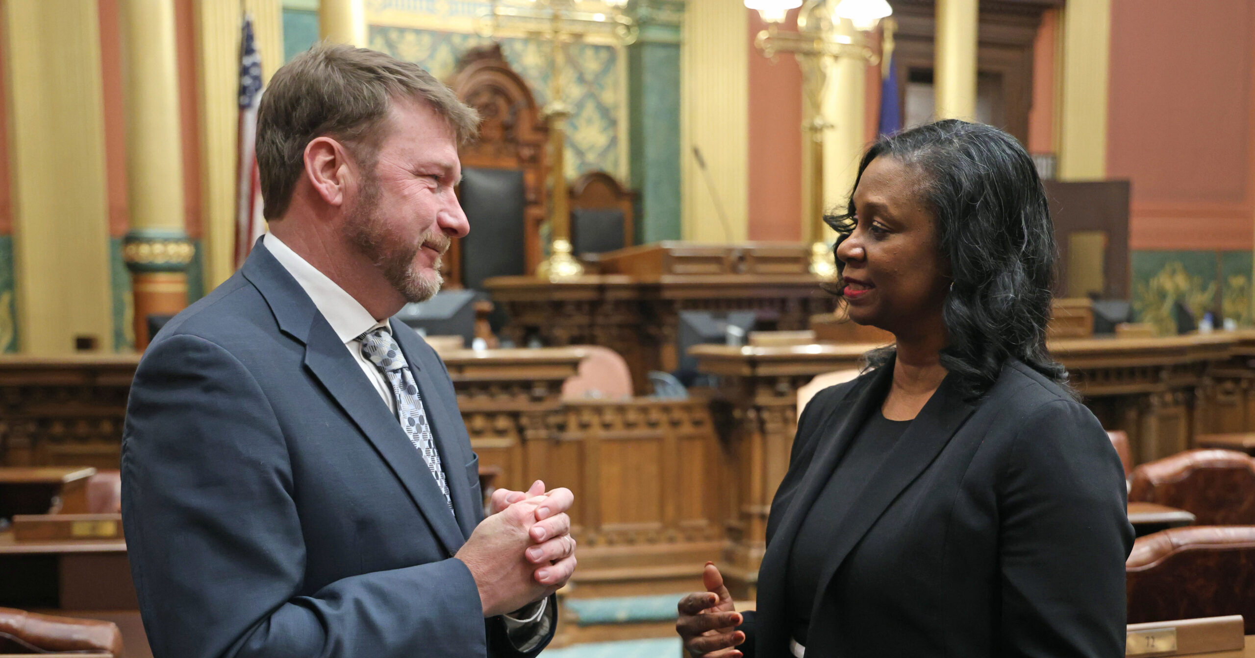 Michigan state Representatives Matt Longjohn and Tonya Myers Phillips speaking with one another on the House floor.