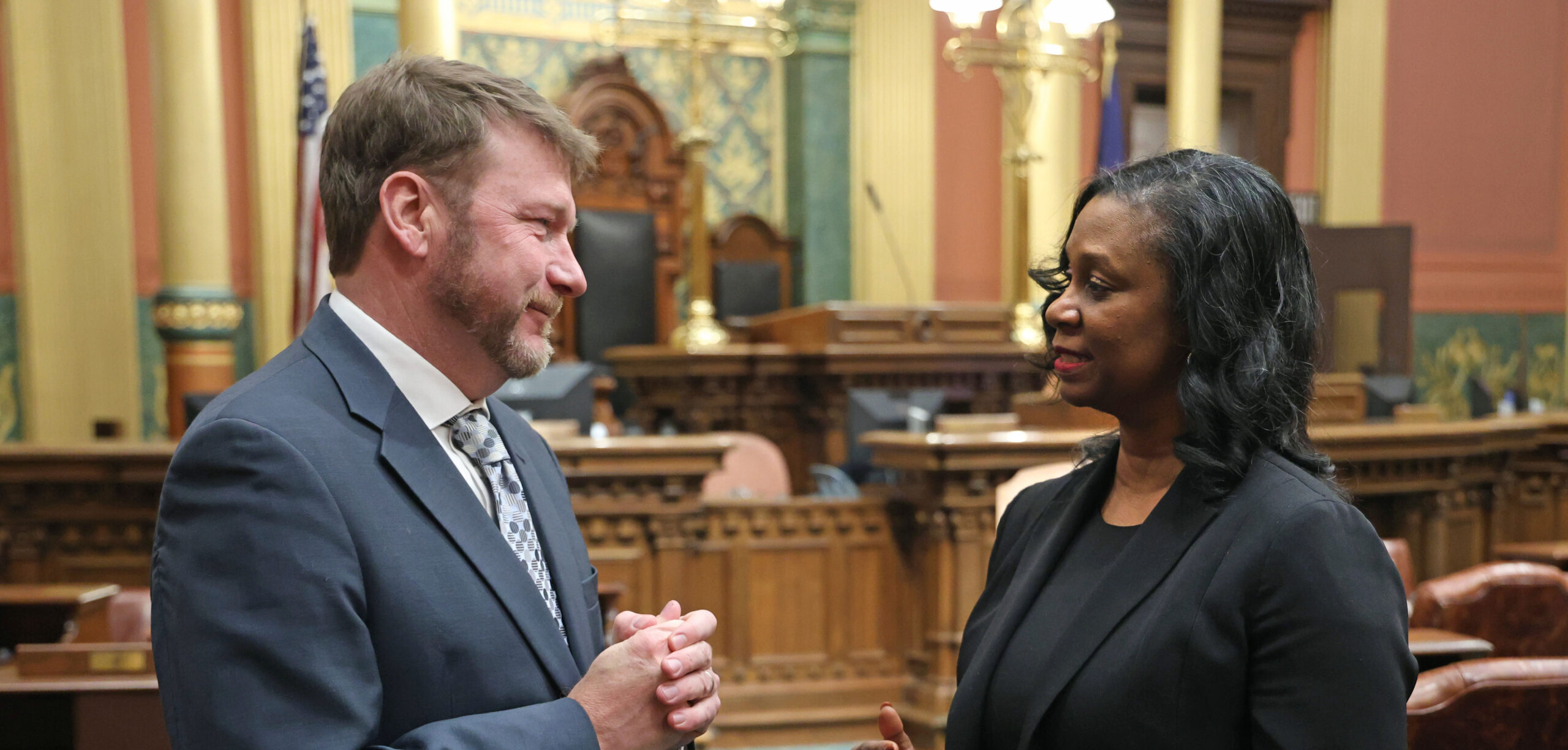 Michigan state Representatives Matt Longjohn and Tonya Myers Phillips speaking with one another on the House floor.