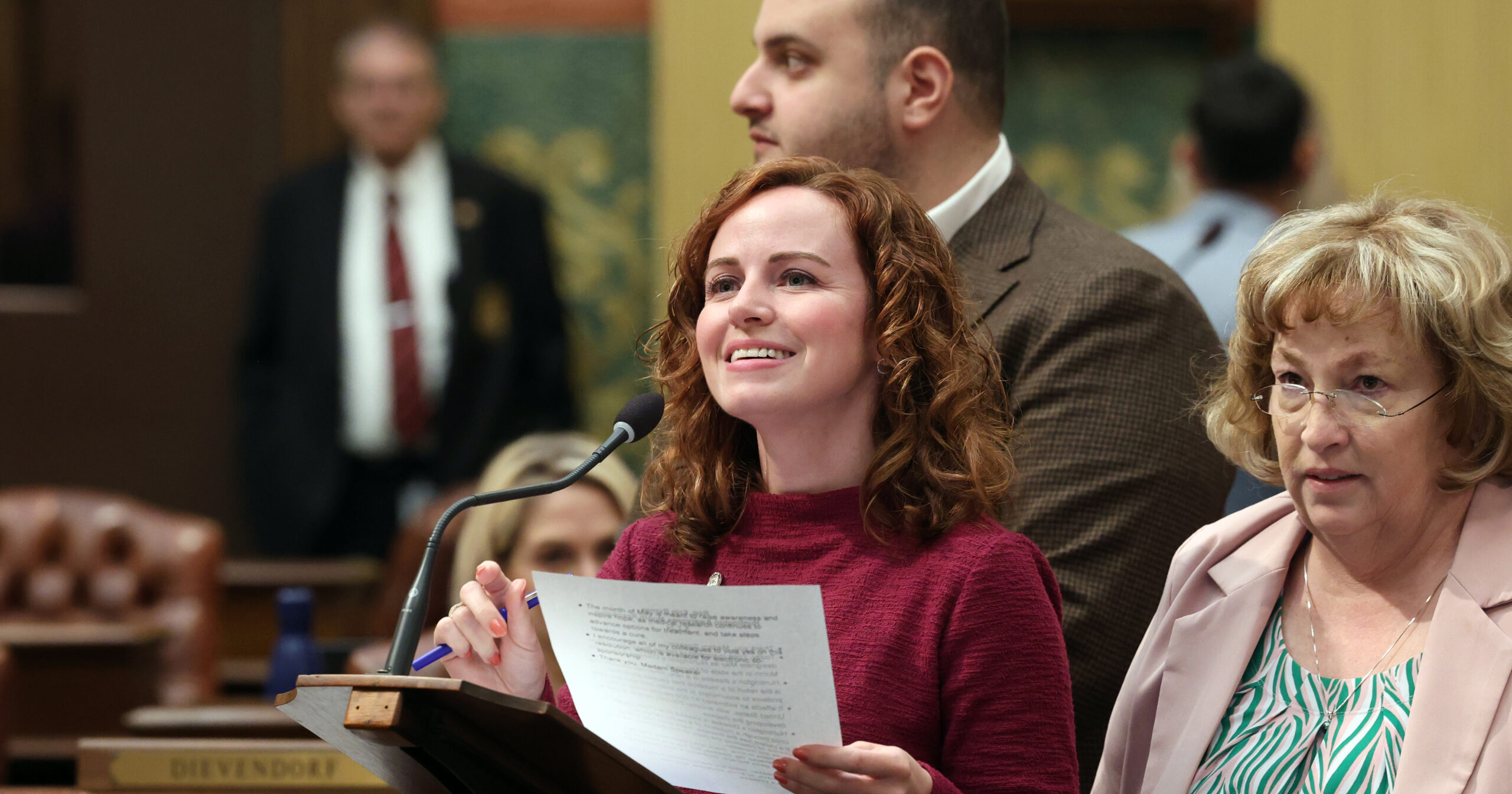 Michigan State Representative Erin Byrnes delivers a floor speech on the House Floor while standing behind a podium accompanied by her colleagues.