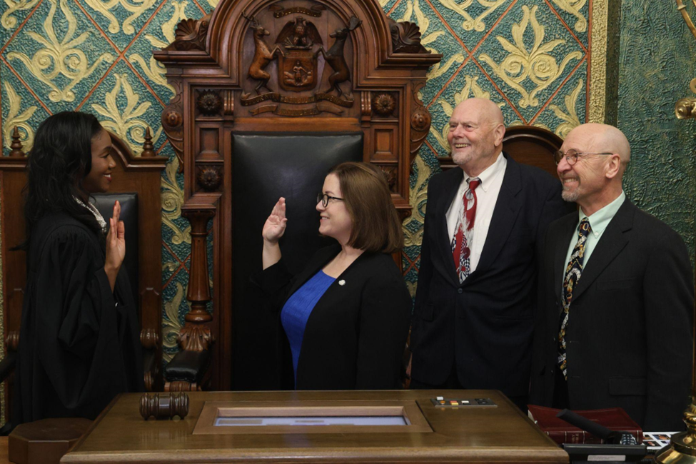 Michigan State Representative Natalie Price stands with her hand raised while being sworn into the 103rd Legislature by Michigan Supreme Court Justice Kyra Harris Bolden.