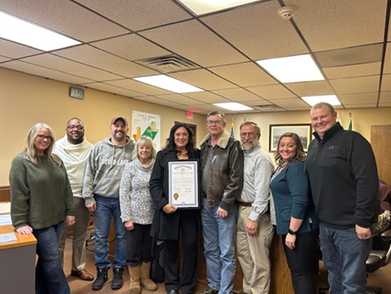 Michigan State Representative Angela Witwer standing with members of the Village of Dimondale Council holding a retirement tribute certificate for Bill Bowers.