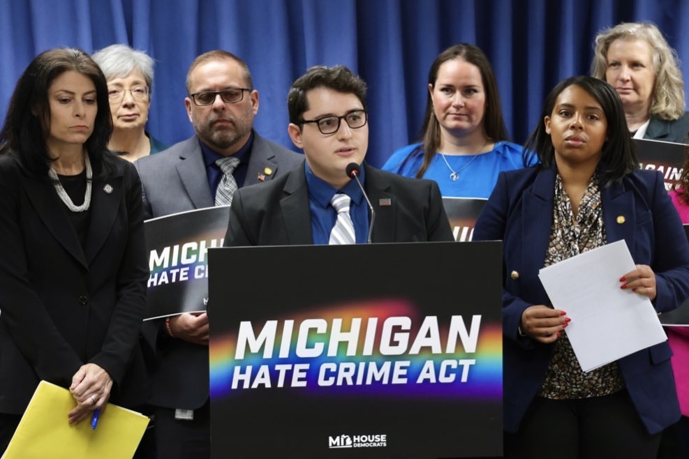 Michigan State Representative Noah Arbit speaking at a press conference behind a podium that reads "Michigan Hate Crime Act."