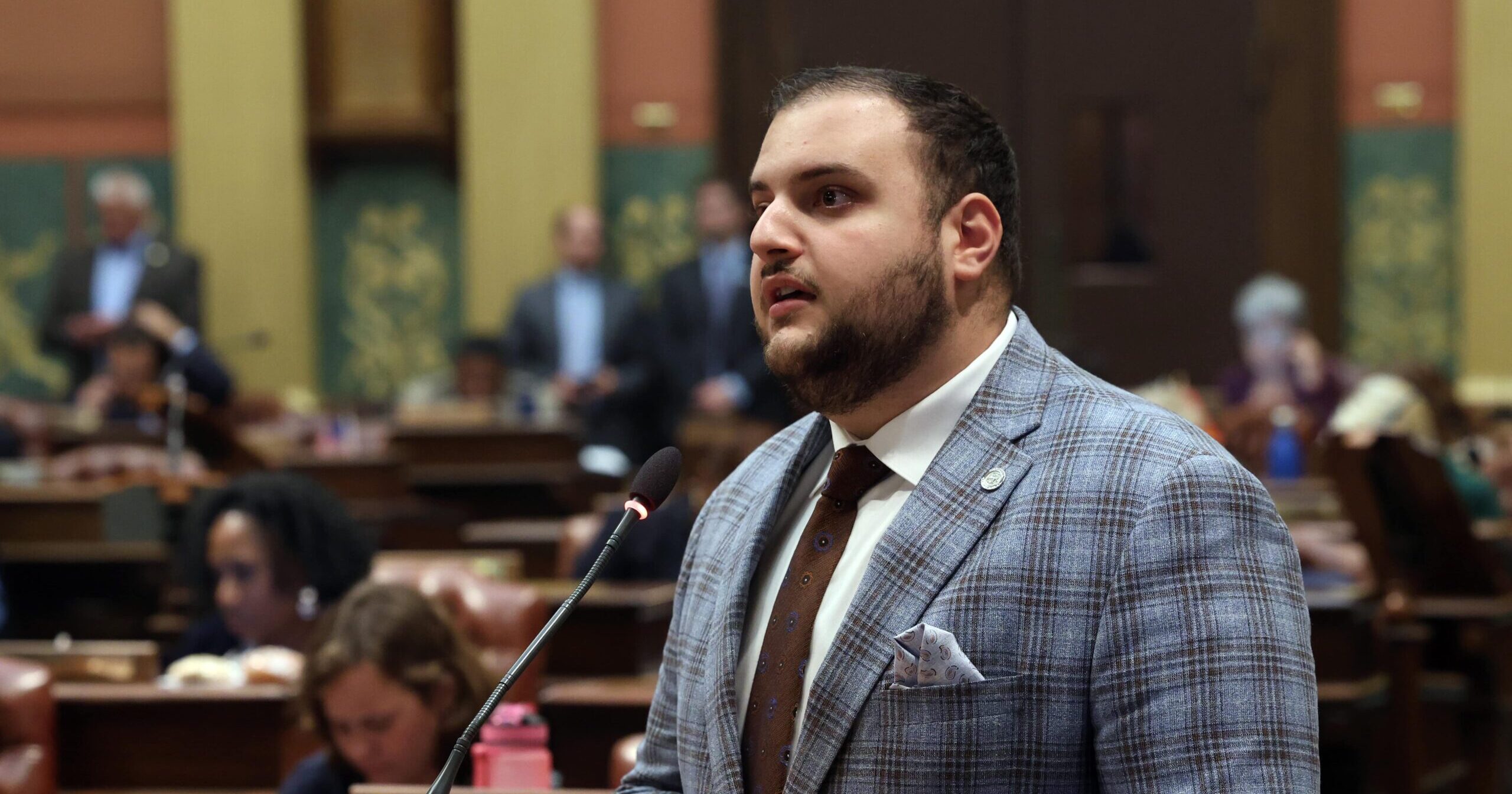 Michigan State Representative Alabas Farhat speaking behind a podium on the House Floor.