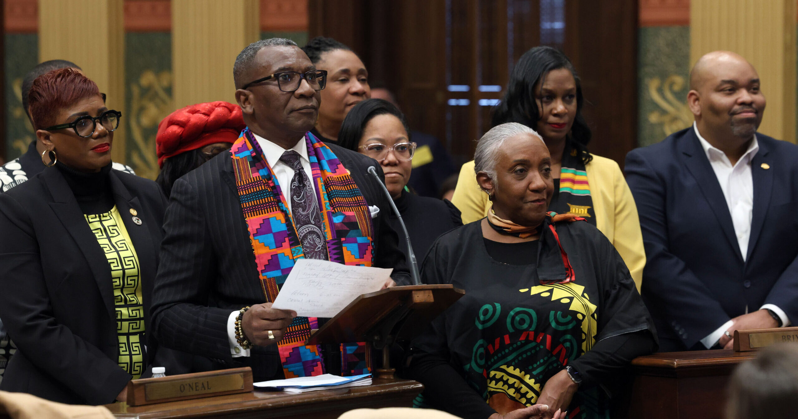 Image of Michigan state Rep. Amos O'Neal speaking on the House floor surrounded by his colleagues.