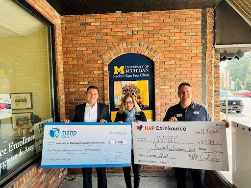 State Rep. Jennifer Conlin holding two checks with representatives from MAHP and HAP CareSource on Friday, April 25, 2025 at the University of Michigan’s Student-Run Free Clinic.