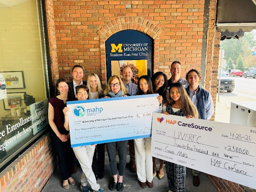 State Rep. Jennifer Conlin standing with a group of people holding two checks from MAHP and HAP CareSource on Friday, April 25, 2025 at the University of Michigan’s Student-Run Free Clinic.