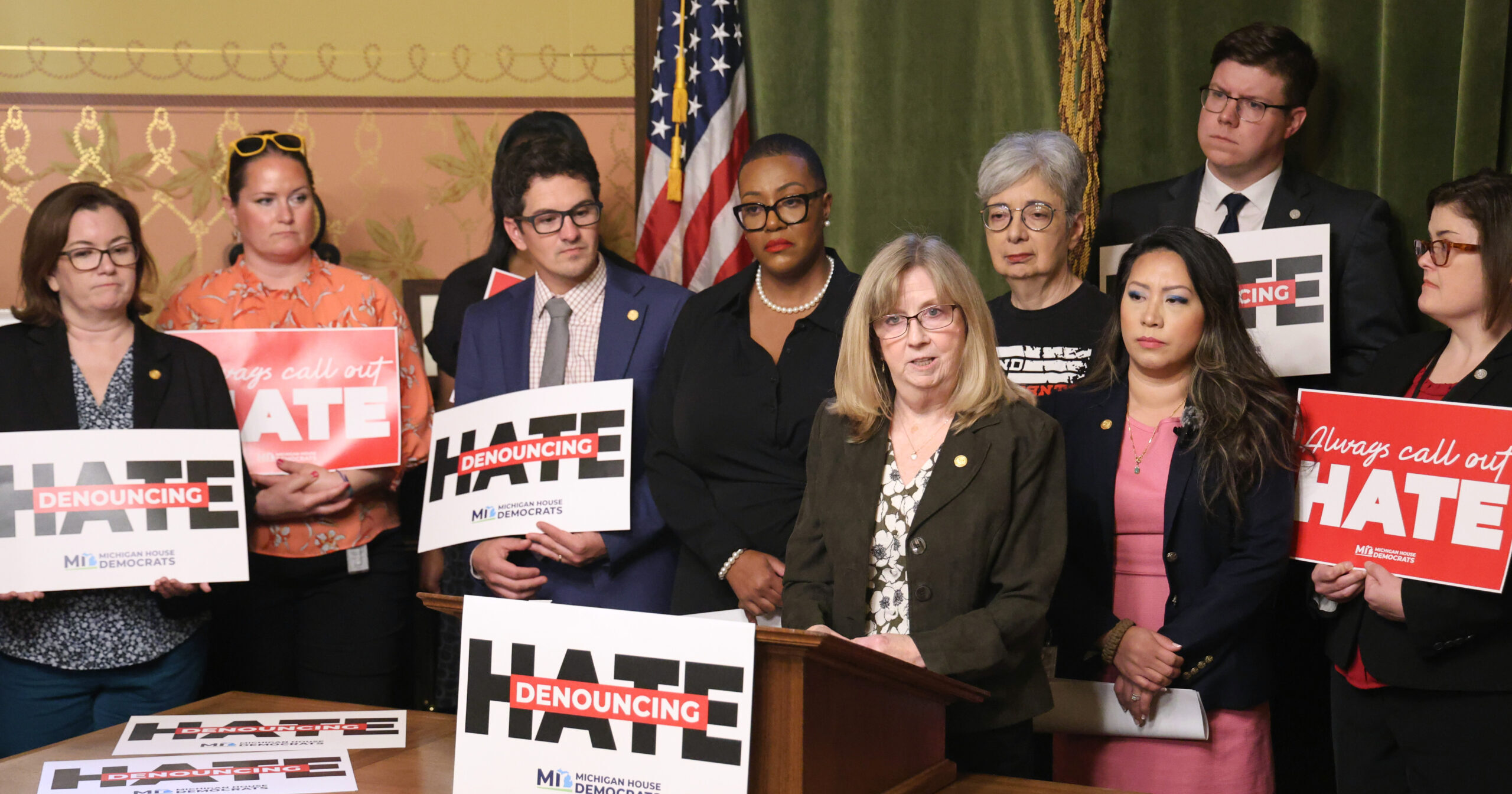 Michigan state Representative Sharon MacDonell speaking at a press conference surrounding by Democratic colleagues holding signs that read "Denouncing Hate."