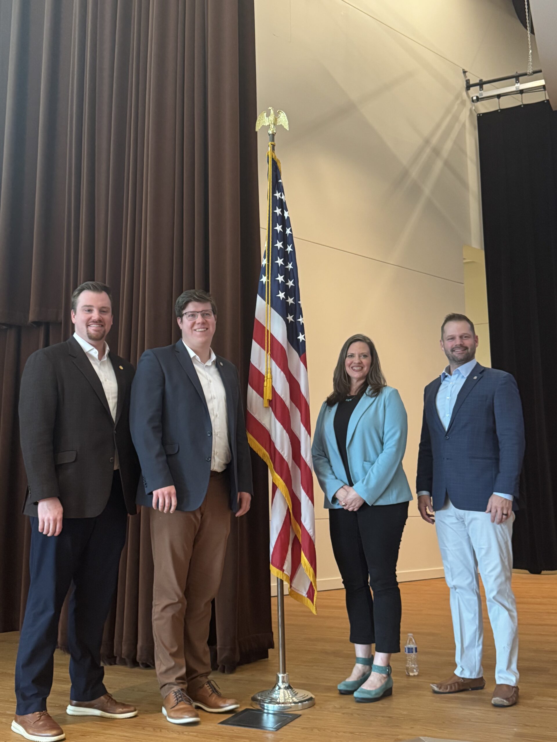 Michigan state Representative John Fitzgerald and colleagues posing for a photo on stage around a United States flag.