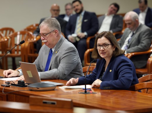Michigan state Representative Natalie Price sitting alongside a colleague while speaking at a committee meeting.