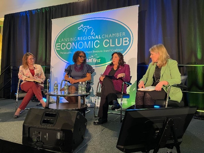 Michigan State Representative Angela Witwer speaking with colleagues on stage in front of a banner that reads "Lansing Regional Chamber Economic Club."