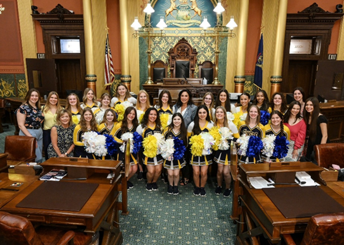 Michigan state Representative Angela Witwer and the Grand Ledge Pompon Junior Varsity and Varsity teams posing for a photo on the House floor.