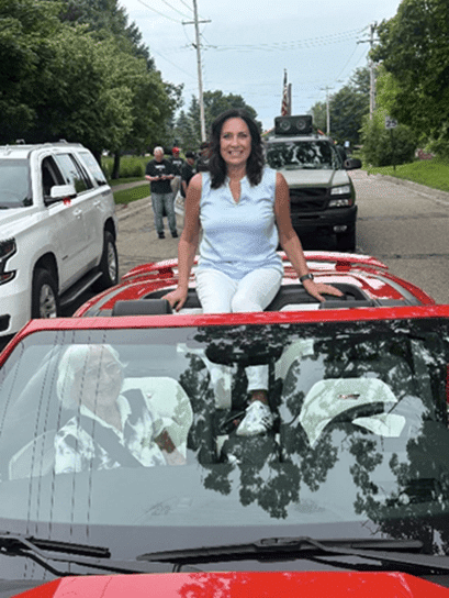 Michigan state Representative Angela Witwer sitting on the hood of a red car in the annual Olivet Firefighter's Association parade.