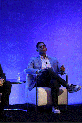 Michigan State Representative Ranjeev Puri sitting on stage at a panel event, speaking. Behind him is a screen with the logo for the 2026 Mackinac Policy Conference.