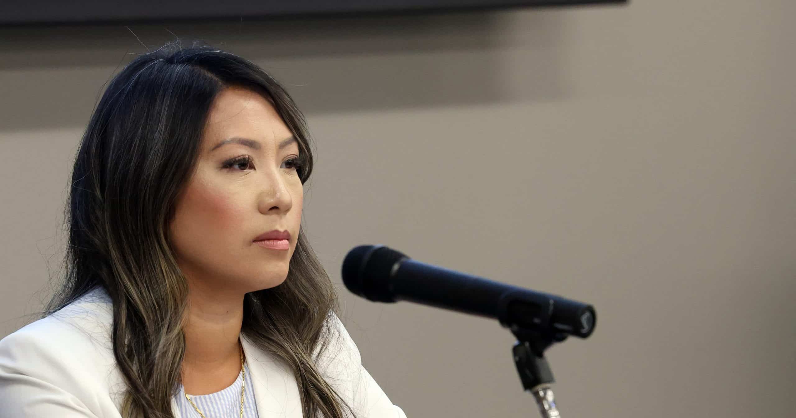 State Representative Mai Xiong speaking behind a microphone at a town hall meeting.